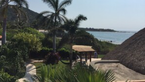 Un complexe hôtelier tropical doté de palmiers, offrant une vue sur la plage et comprenant un bâtiment à toit de chaume.