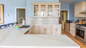 Een ruime keuken met marmeren aanrechtbladen, een groot eiland en lichtblauwe wanden.