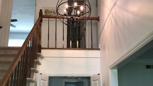 A staircase leading to a second floor with a chandelier, a door leading to another room, and a lamp on a side table. - Carmel Road / Ballantyne  / South Charlotte Area Cape Cod  Home (Charlotte)