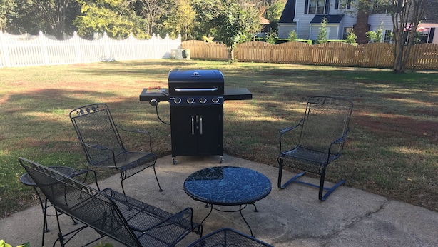 A backyard with a barbecue grill, four metal chairs, and a round table. - Carmel Road / Ballantyne  / South Charlotte Area Cape Cod  Home (Charlotte)