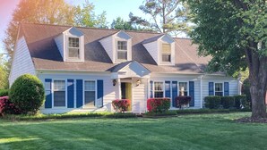 A two-story house with a gabled roof, dormer windows, and a front porch with a small porch light. - Carmel Road / Ballantyne  / South Charlotte Area Cape Cod  Home (Charlotte)