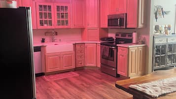 Una cocina con armarios rosados, un refrigerador negro, un microondas y una mesa de madera con un banco.
