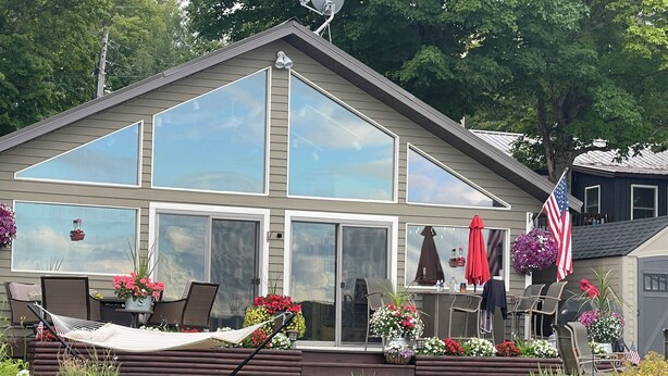 A two-story house with large windows, a deck with outdoor furniture, and a garden with various plants and flowers. - Hayward, Wisconsin Waterfront Cabin located on Nelson Lake, Pontoon available. (Hayward)