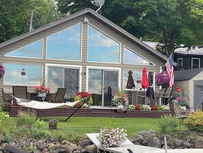 A two-story house with large windows, a deck with outdoor furniture, and a garden with various plants and flowers. - Hayward, Wisconsin Waterfront Cabin located on Nelson Lake, Pontoon available. (Hayward)