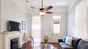 A living room with a fireplace, a television, a sofa, a coffee table, and a ceiling fan. - Large Shotgun Double In Perfect Uptown Location Near Magazine and State St. (New Orleans)