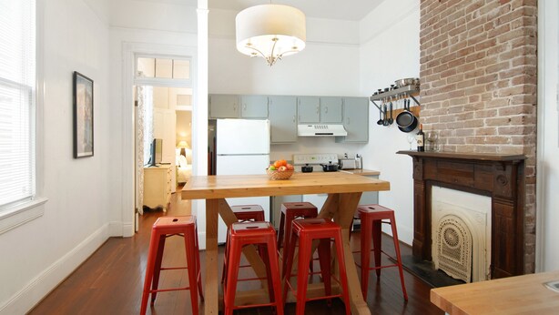 A kitchen with a wooden island, red barstools, a brick fireplace, and a hanging pot rack. - Large Shotgun Double In Perfect Uptown Location Near Magazine and State St. (New Orleans)