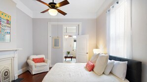 A bedroom with a large bed, a ceiling fan, a fireplace, and a view of the hallway. - Large Shotgun Double In Perfect Uptown Location Near Magazine and State St. (New Orleans)