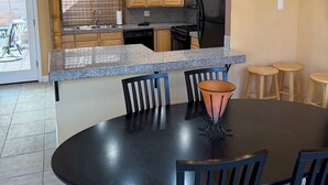 Uma cozinha moderna com armários de madeira, bancada de granito e uma área de refeições com mesa e cadeiras pretas.