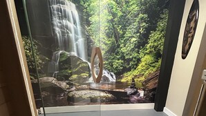 A shower area with a glass door, a wooden door frame, and a view of a waterfall through the glass. - Urban Retreat! Sauna-Updated Craftsman Private Backyard! Pet friendly! Discounts (Seattle)