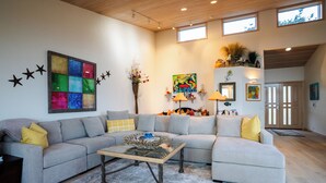 A modern living room with a sectional sofa, a glass coffee table, and a colorful abstract painting. - Inspired by a view of the Sea (Sea Ranch)