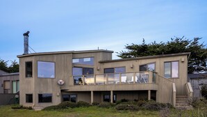 A modern two-story house with a flat roof, large windows, and a visible chimney. - Inspired by a view of the Sea (Sea Ranch)