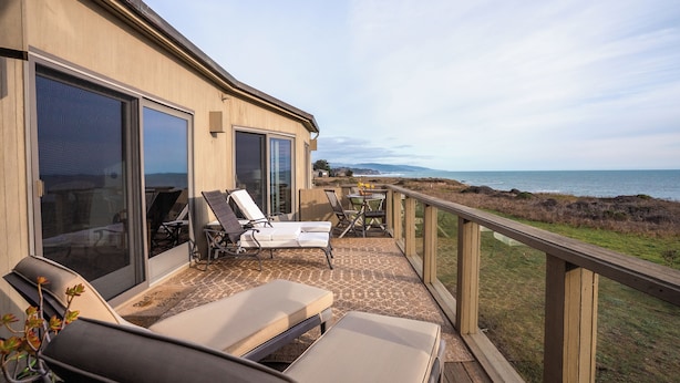 A balcony with sun loungers and a table, overlooking a coastal view. - Inspired by a view of the Sea (Sea Ranch)