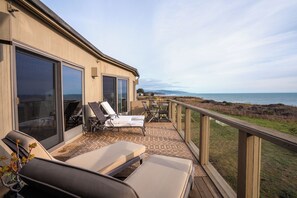 A balcony with sun loungers and a table, overlooking a coastal view. - Stunning Sea Ranch Oceanfront Home! Panoramic Views & Whale Watching! (Sea Ranch)