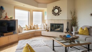 A living room with a television, seating area, fireplace, and large windows overlooking the sea. - Inspired by a view of the Sea (Sea Ranch)