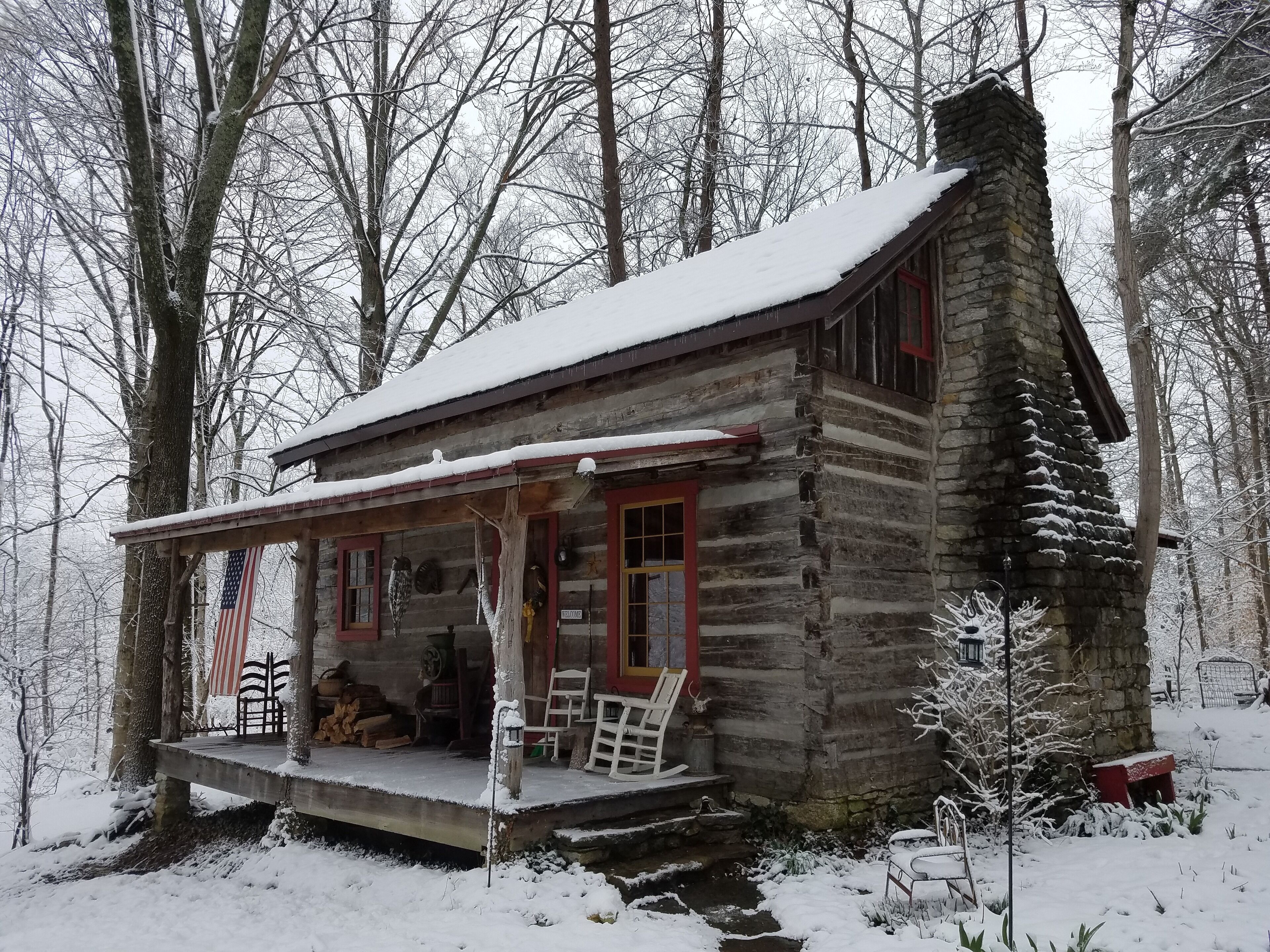 Une cabane en rondins avec un porche, entourée d’arbres couverts de neige.