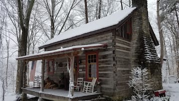 Une cabane en rondins avec un porche, entourée d’arbres couverts de neige.