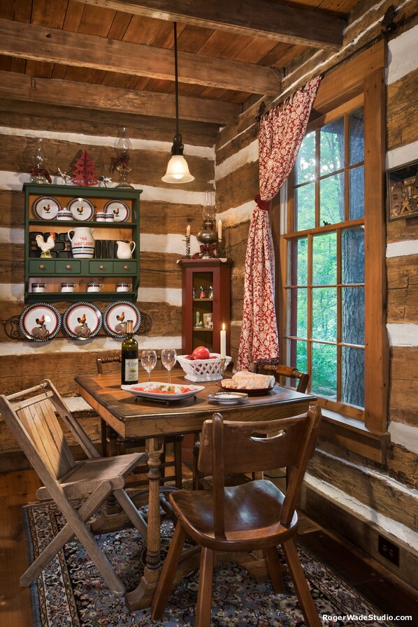 A rustic wooden cabin interior with a dining table, chairs, a chandelier, and a window with curtains. - Captain's Cabin Bed & Breakfast: Bourbon Trail. History & Romance (Louisville)