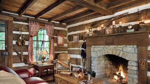 Un acogedor interior de cabaña de troncos con chimenea de piedra, muebles de cuero y decoración rústica.