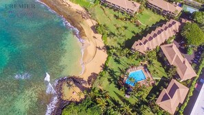 Vista aérea de un complejo turístico con playa, piscina y varias edificaciones con tejados diferentes.