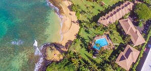Vista aérea de un complejo turístico con playa, piscina y varias edificaciones con tejados diferentes.