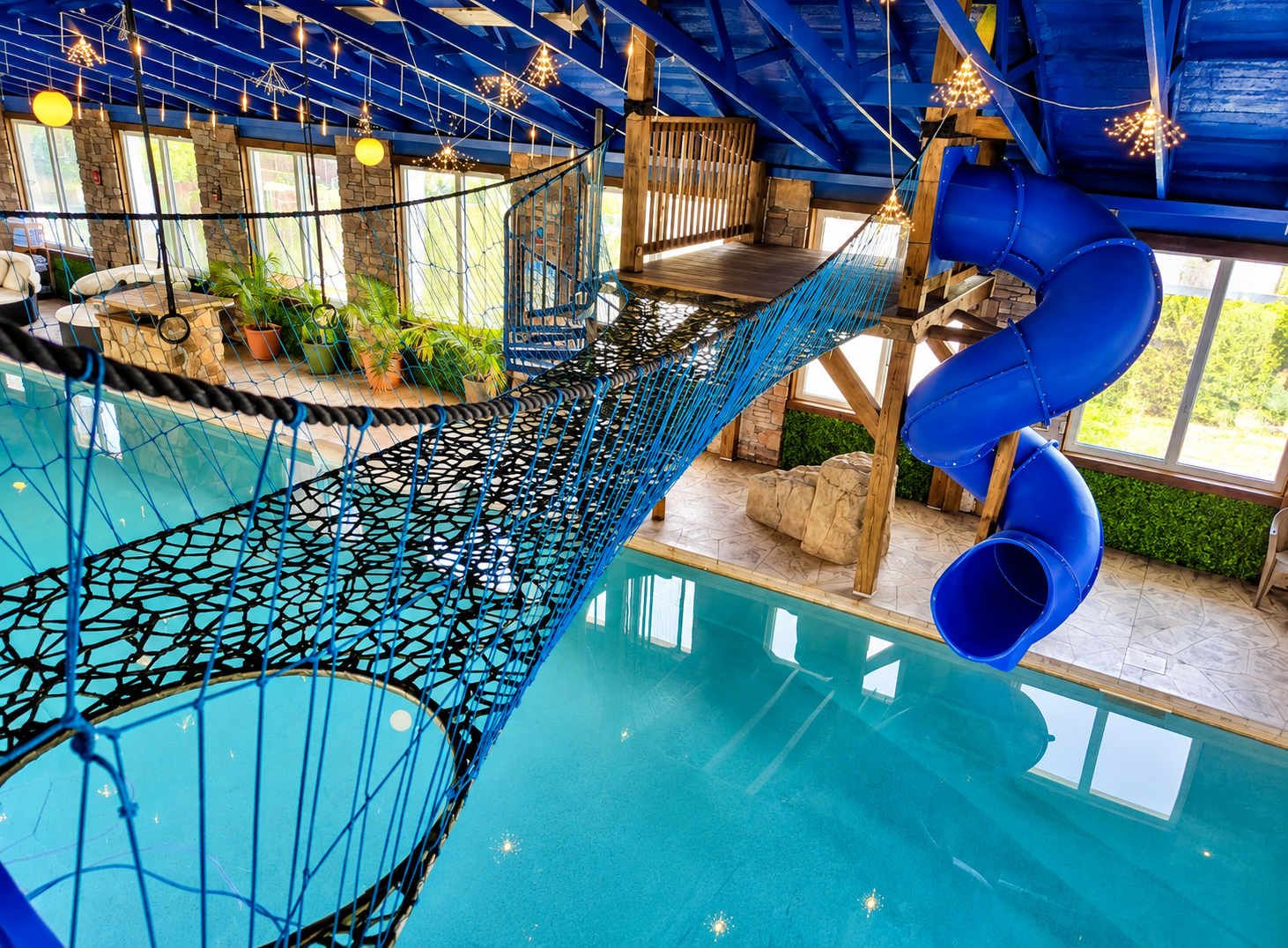 Un espace piscine équipé d’un pont de corde, de toboggans et de structures en bois.