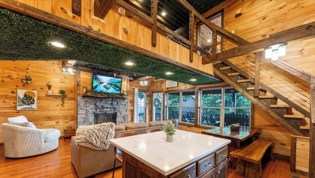 A spacious living area with a stone fireplace, wooden ceiling, and a large TV. - Big Time Hill Cabin with an indoor pool, hot tub, & great views! (Bryant)