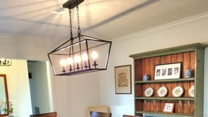 A dining room with a wooden table and chairs, a hanging light fixture, and a wooden cabinet with decorative plates. - Fishing Tournaments, Auburn Games (Alexander City)