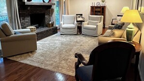 A living room with a fireplace, two white armchairs, a sofa, a wooden coffee table, and a lamp. - Fishing Tournaments, Auburn Games (Alexander City)