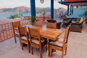 A wooden dining table with chairs, a poolside area, and a view of the sea.