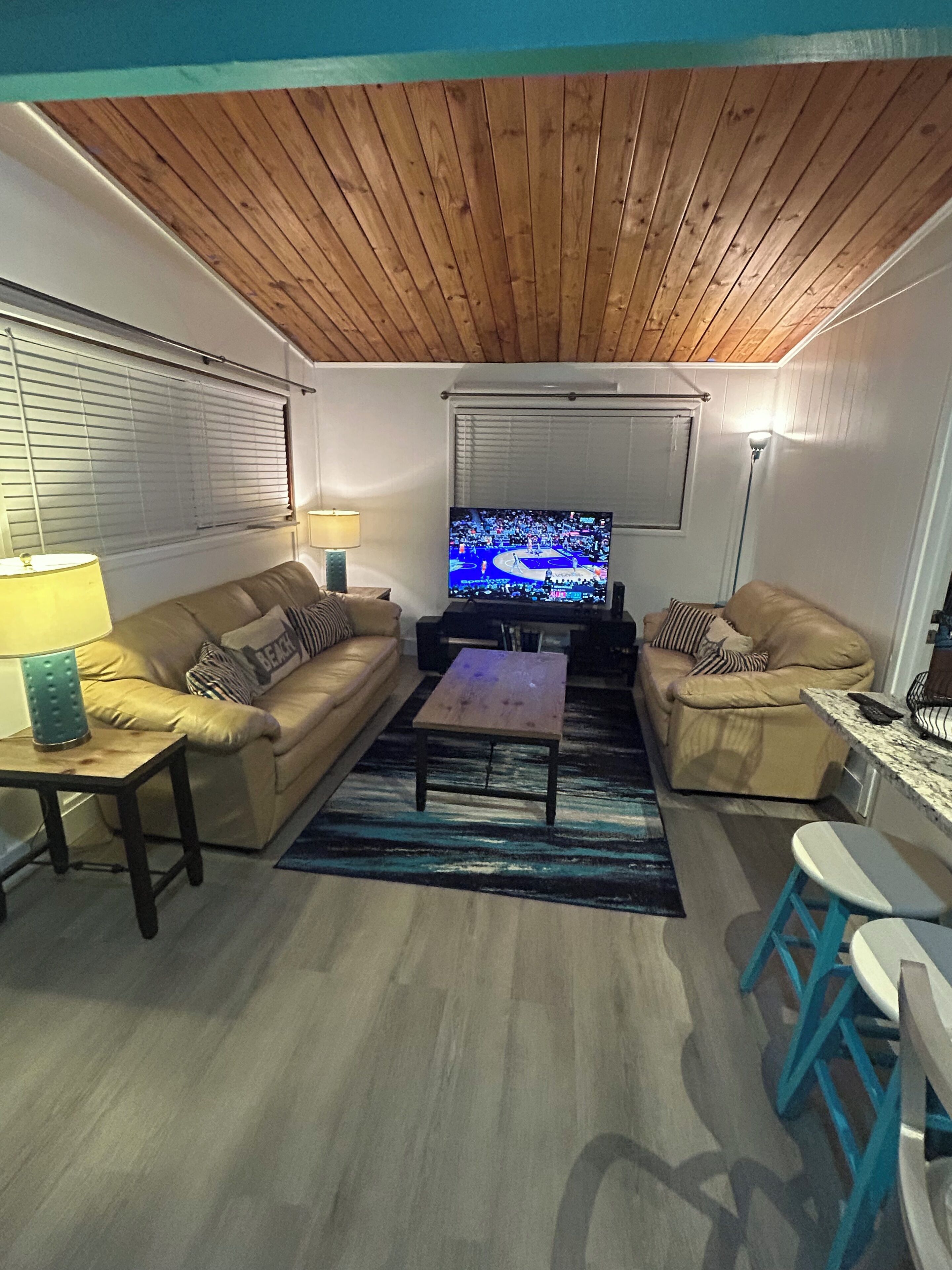 A living room with two sofas, a coffee table, a TV, and a bar area with stools.