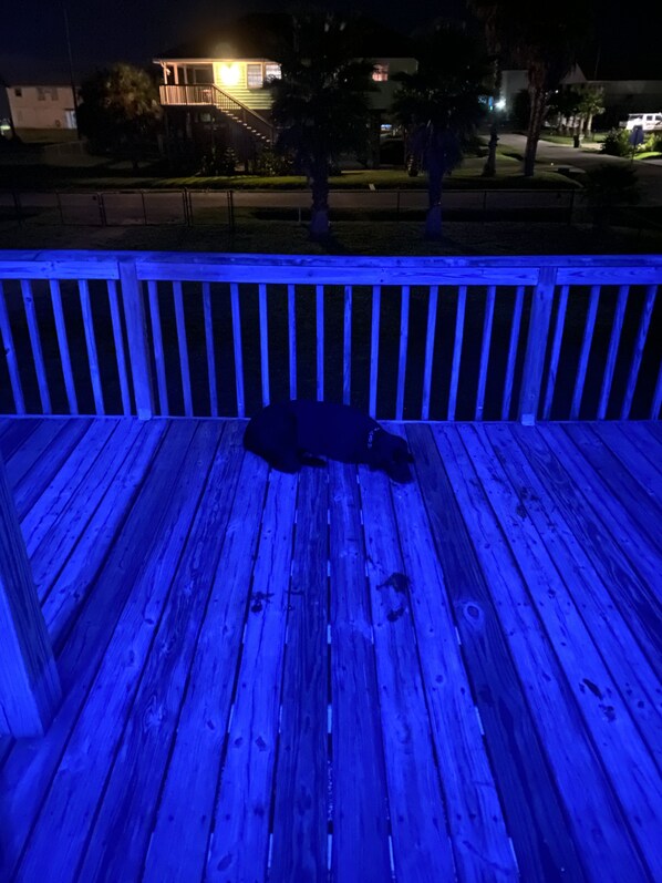 Une terrasse en bois avec une balustrade, un banc et un escalier menant à un bâtiment dont une fenêtre en forme de cœur est illuminée.