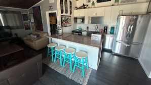 Una cucina moderna con mobili bianchi, un frigorifero in acciaio inossidabile e un angolo bar con sgabelli color turchese.