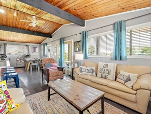 Un vaste espace de vie doté d’un plafond en bois, d’un canapé beige agrémenté de coussins aux motifs marins, d’une table basse et d’un tapis à motifs.