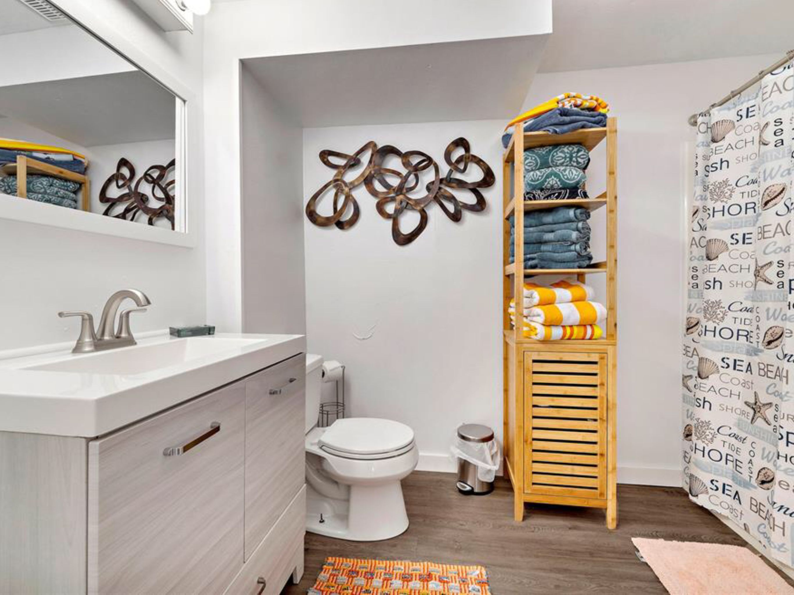 A modern bathroom with a white sink, toilet, and shower curtain with a beach theme.