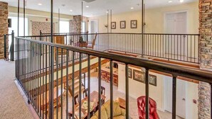 Un interior espacioso con un techo alto, una escalera con barandilla metálica y un comedor con mobiliario de madera.