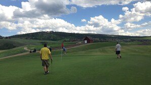 A golf course with a red flag, a golf cart, and a small building in the background. - Enjoy the Summer at Granby Ranch.  Golf, Bike, Hike, Fish the Fraser River! (Granby)