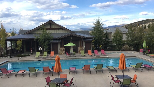 A pool area with lounge chairs and umbrellas, a building with a sloped roof, and a mountainous backdrop. - Enjoy the Summer at Granby Ranch.  Golf, Bike, Hike, Fish the Fraser River! (Granby)