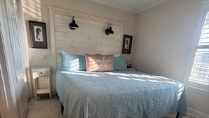 Un dormitorio con cama, mesita de noche, ventilador de techo y ventana con persianas.