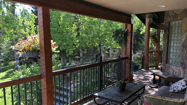 A covered outdoor deck with a wooden railing, a bench, and a stone wall.