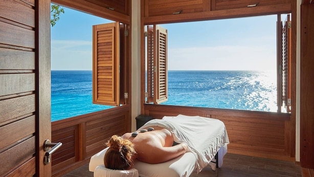 A spa room with a wooden interior, a massage table, and a view of the ocean.