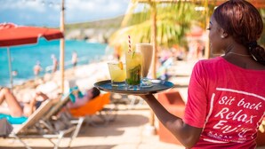 A person holding a tray with drinks at a beachside location.