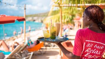 A person holding a tray with drinks at a beachside location.