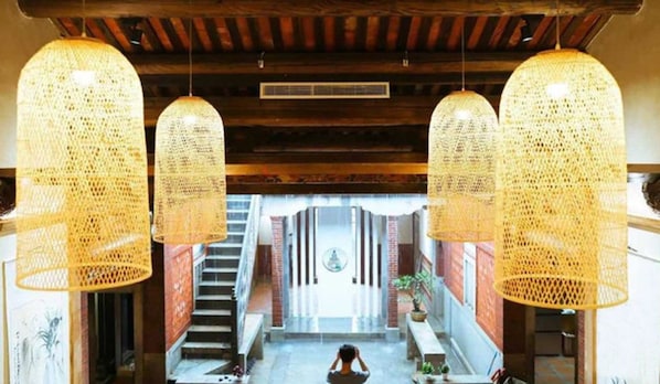 Un intérieur spacieux avec un escalier menant à un espace central, agrémenté de grandes suspensions en fibres tressées et d’un ventilateur de plafond visible.