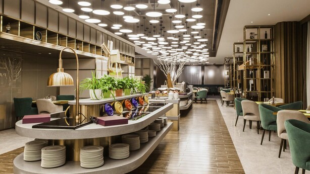 A modern restaurant with a curved counter, multiple seating areas, and a ceiling with circular lights. - Mercure Harbin Songbei (Harbin)