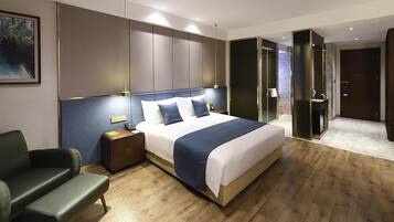 Una habitación de hotel moderna con una cama grande, mesitas de noche, una zona de estar y un baño con ducha de vidrio.