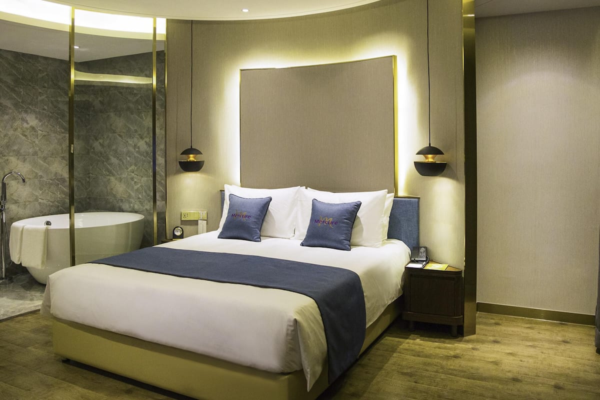 Habitación de hotel moderna con una cama grande, mesitas de noche, ducha integrada y pared de mármol.