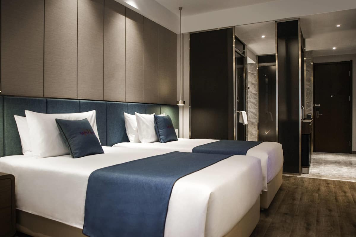 Una habitación de hotel moderna con una cama grande, un área de descanso separada y un baño visible a través de una puerta abierta.