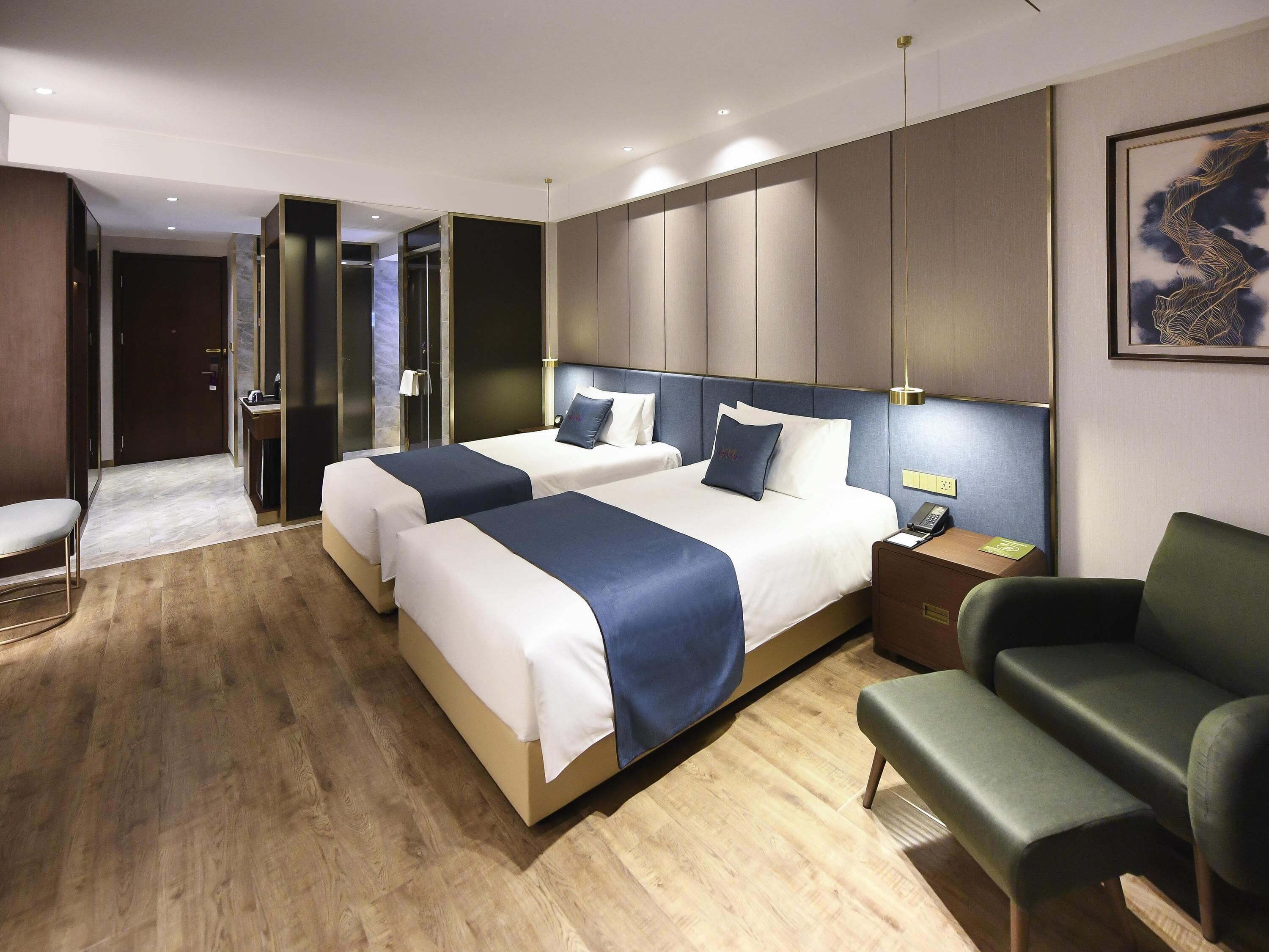 A hotel room with two beds, a desk, a chair, and a bathroom.