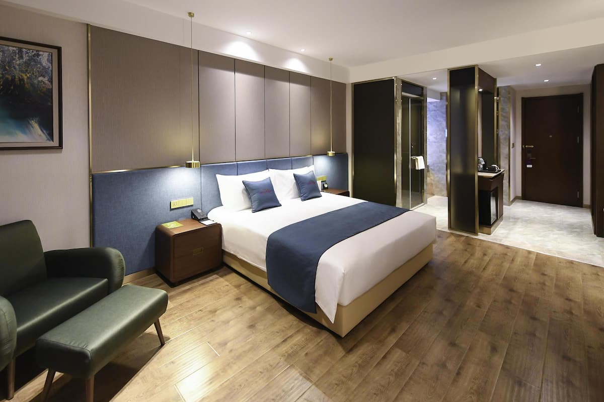 Una habitación de hotel moderna con una cama grande, mesitas de noche, una zona de estar y un baño con ducha de vidrio.