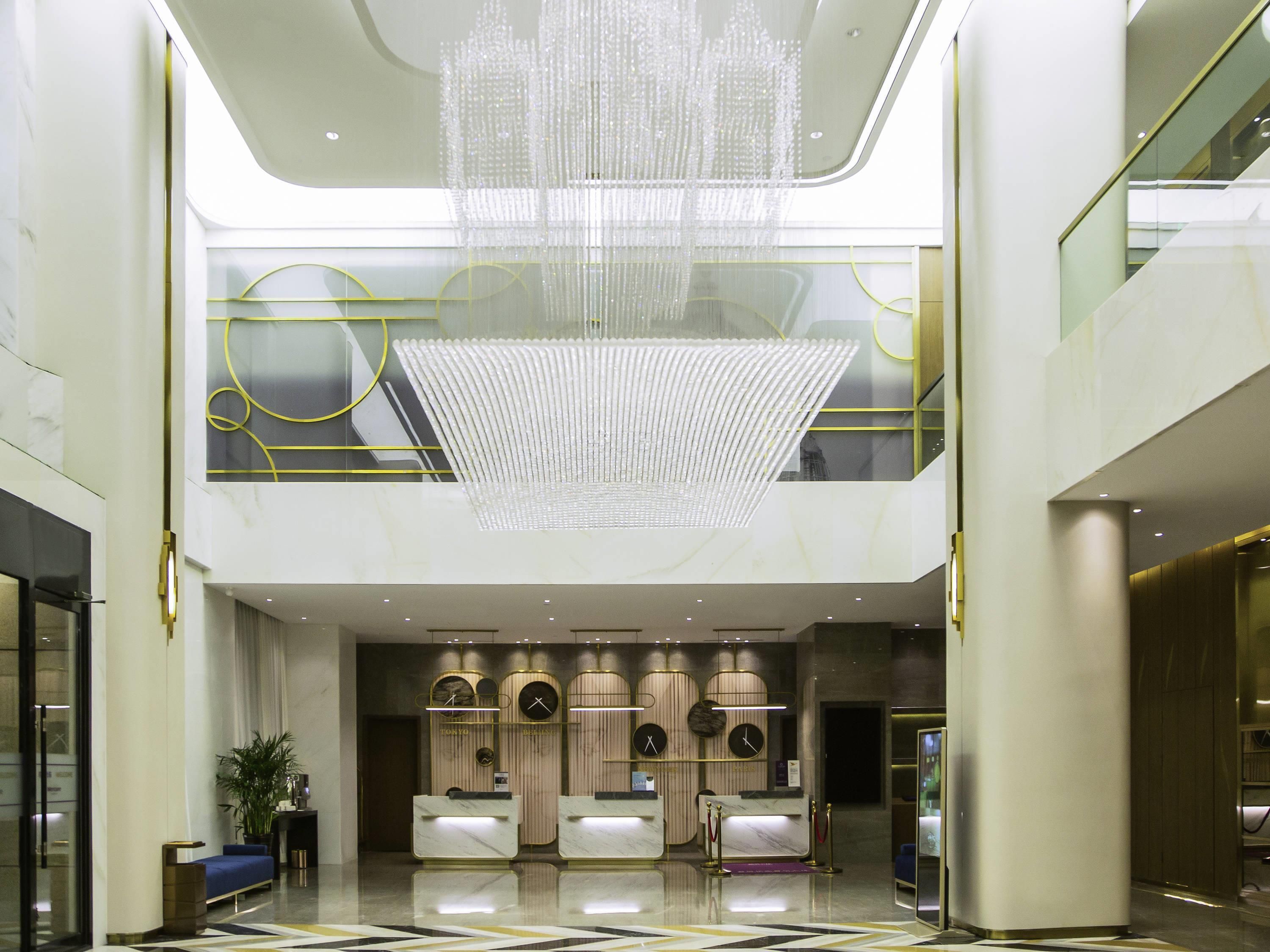 Un hall d’hôtel moderne avec un comptoir d’accueil, un lustre et un plafond haut.